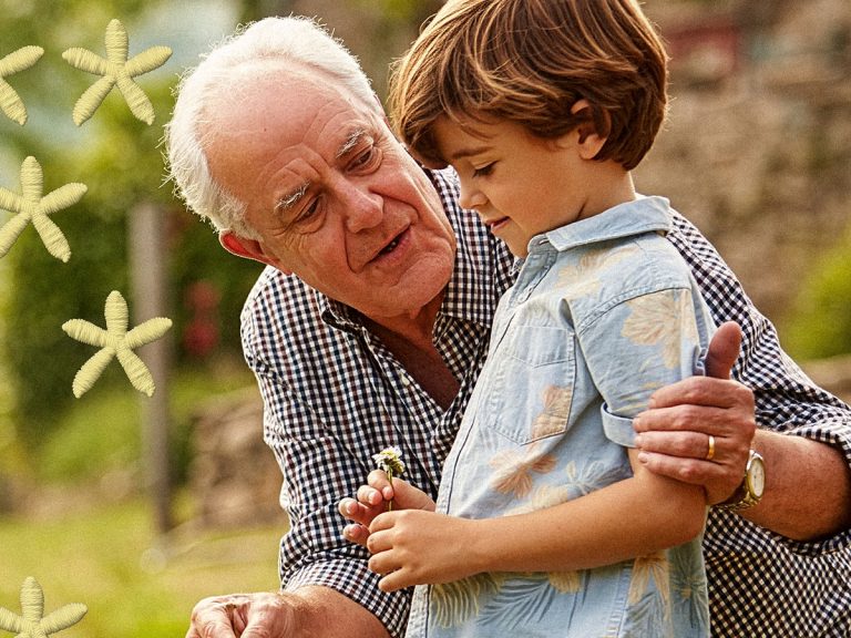 Elderly man talking to young child holding a dandelion.