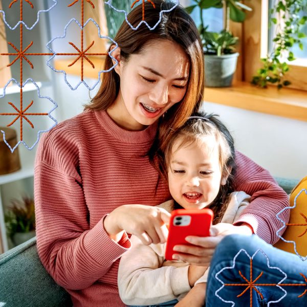 Child sitting on mother's lap, smiling while both looking at a smart phone